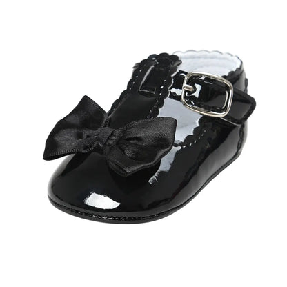 Side angle view of a single baby girl black patent leather T-strap dress shoe with a decorative black satin ribbon bow.