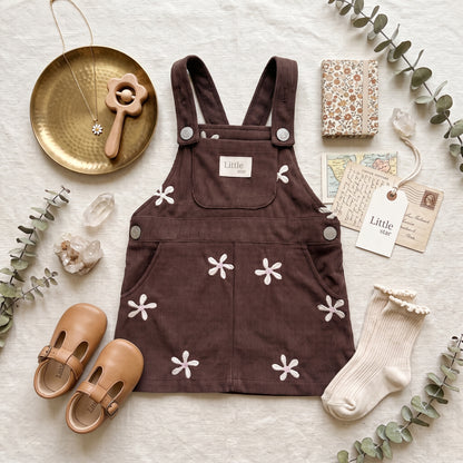 Flat lay arrangement of the brown floral corduroy pinafore dress paired with baby shoes and accessories.