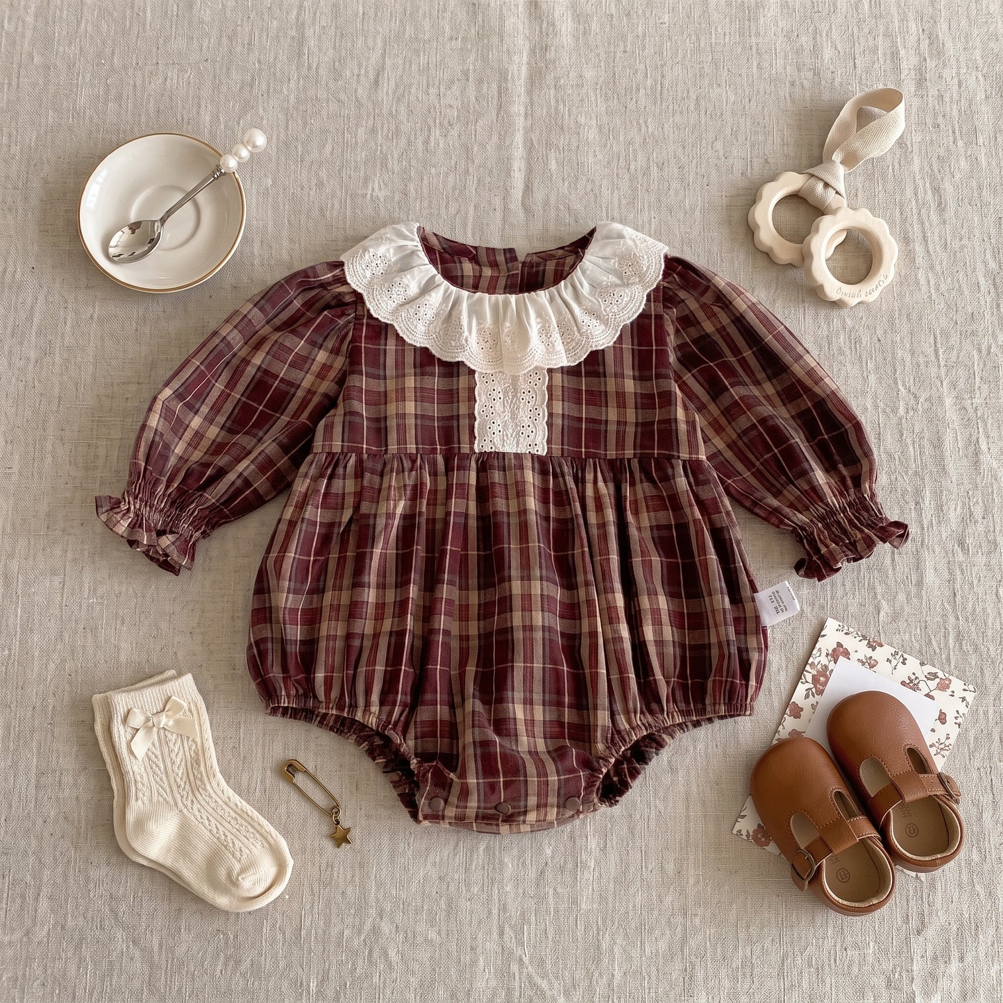 Flat lay of a long sleeve brown plaid baby girl romper styled with cream socks, leather shoes, and accessories.