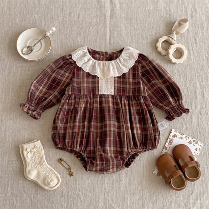 Flat lay of a long sleeve brown plaid baby girl romper styled with cream socks, leather shoes, and accessories.