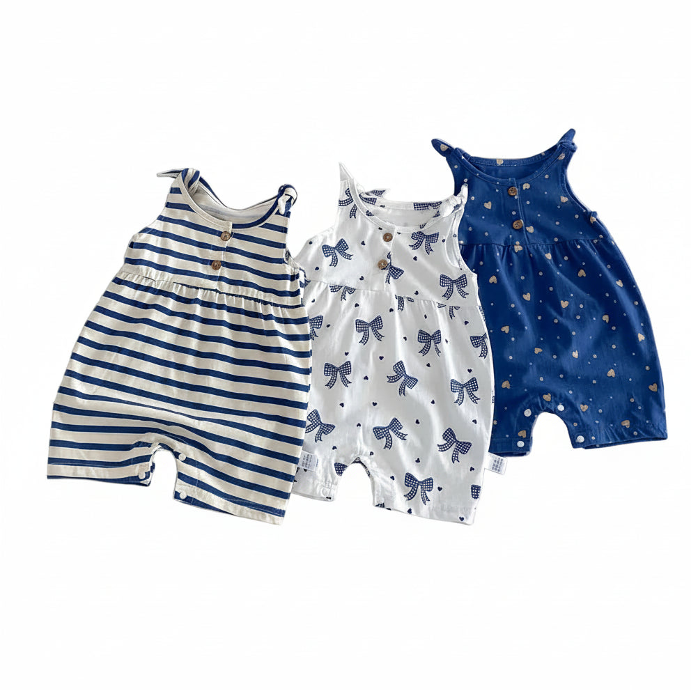 Three baby girl summer rompers in bow print, striped, and blue heart patterns hanging on wooden hangers.
