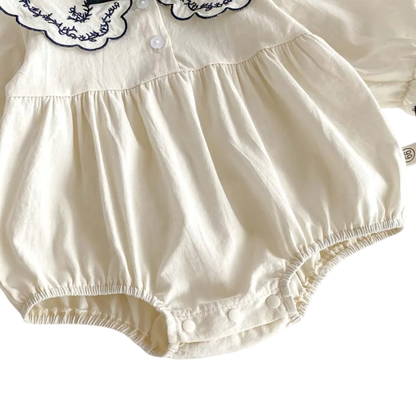 Close-up shot of the elasticated leg opening and fine gathered fabric on the ivory baby romper.