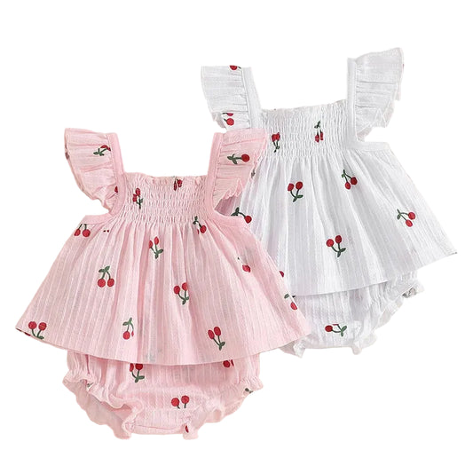 Two baby outfits, one pink and one white, with cherry patterns on a beige background.