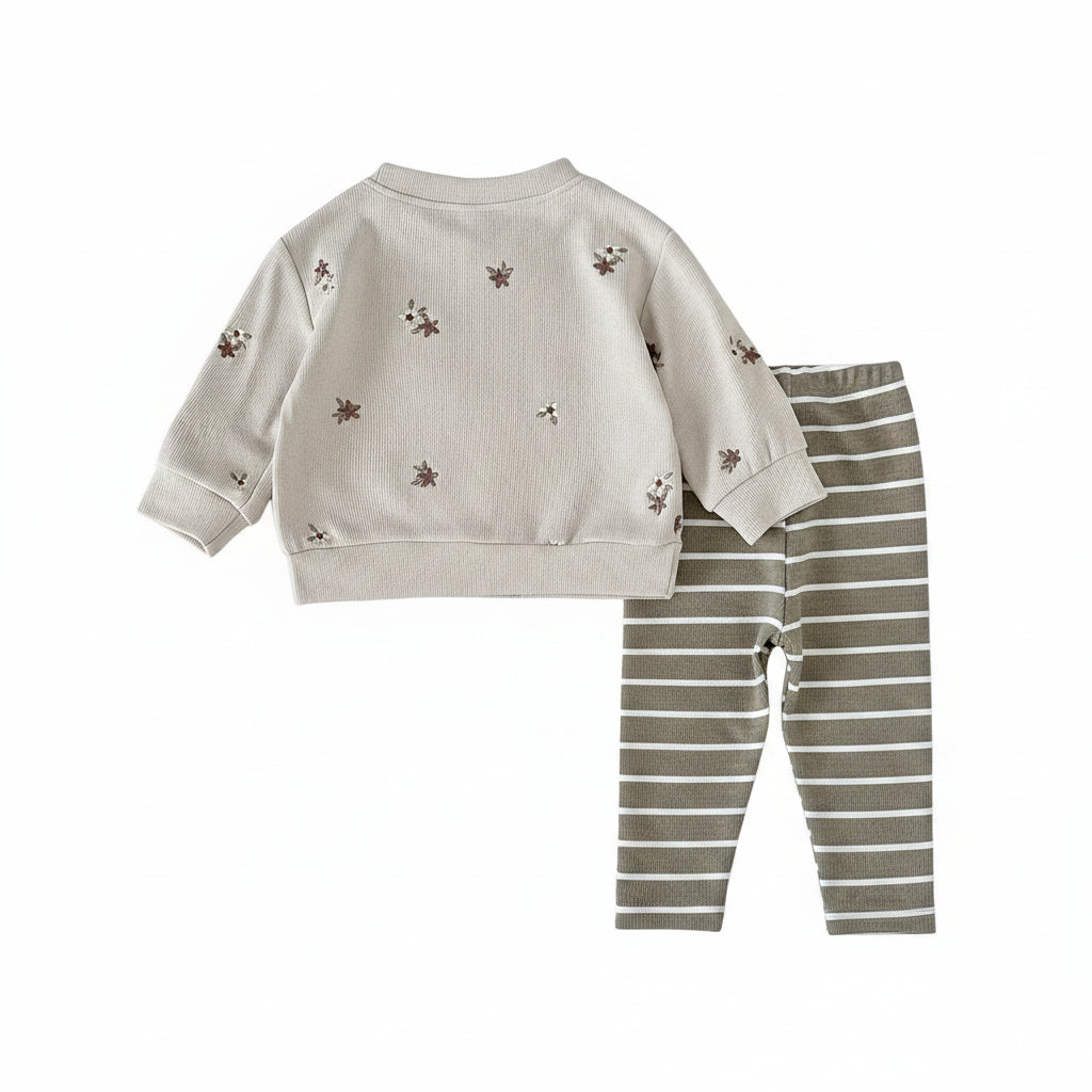 Flat lay of a baby girl's matching outfit set with a long-sleeve cream floral pullover and olive green striped pants.