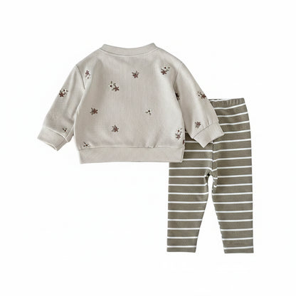 Flat lay of a baby girl's matching outfit set with a long-sleeve cream floral pullover and olive green striped pants.