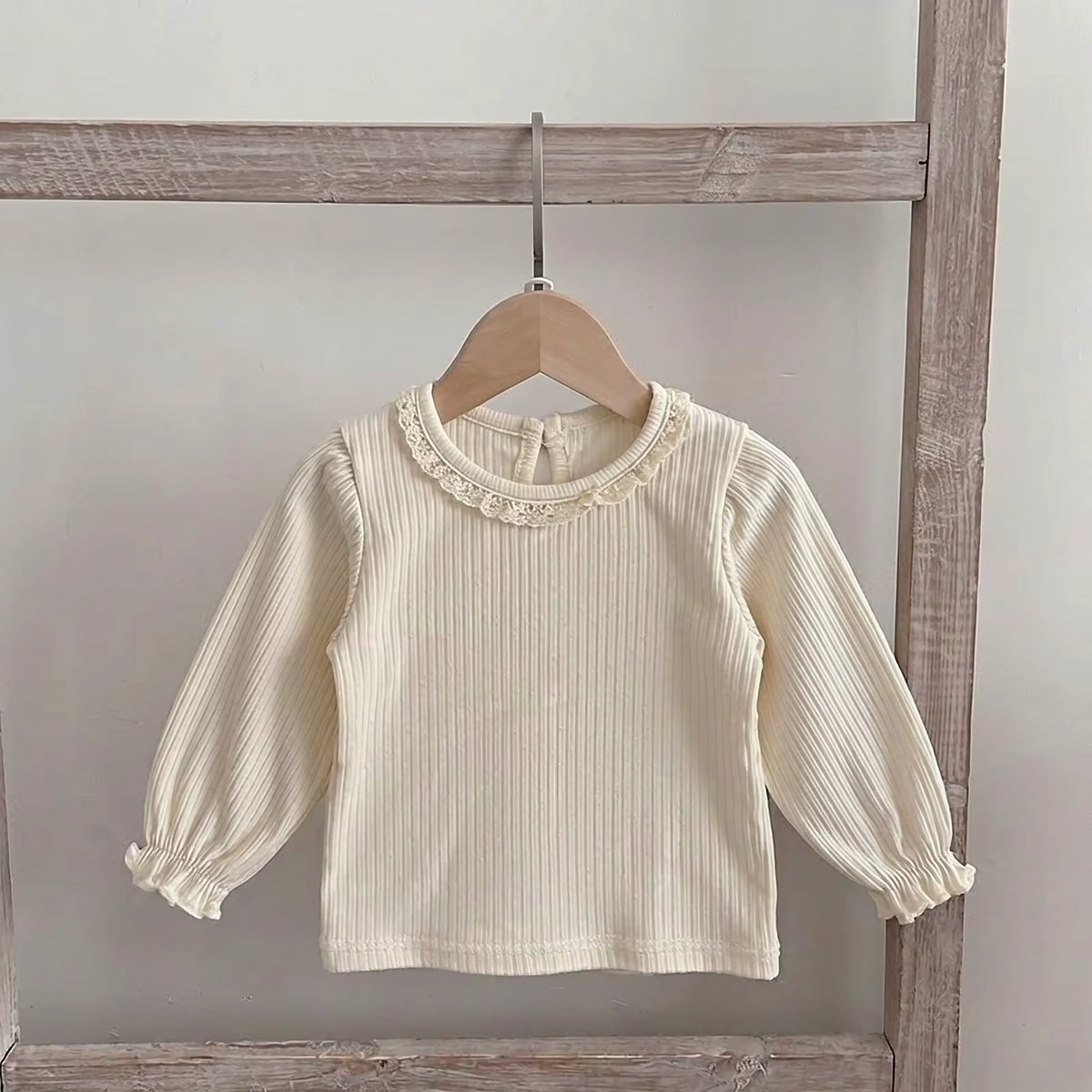 Cream long-sleeve ribbed top with ruffled wrist cuffs and neck trim hanging on a wooden rack