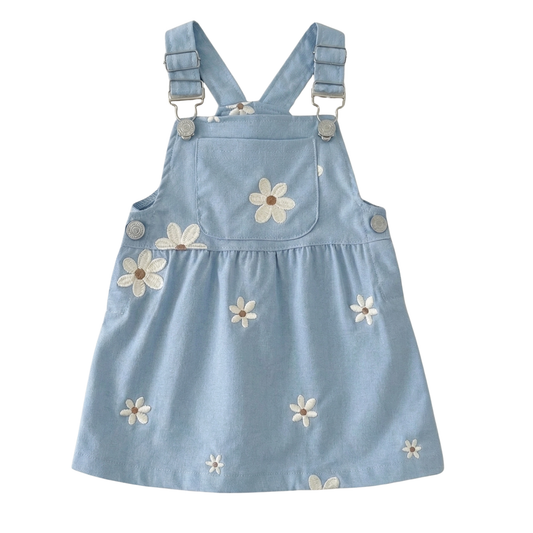 Flat lay of a light blue toddler girl overall dress with white daisy embroidery and adjustable metal buckles on a white background.