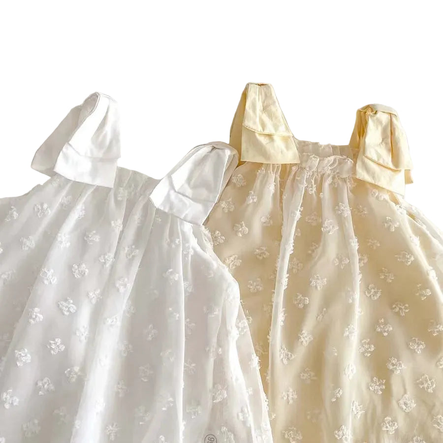 Detail shot of the white and cream bow-tie shoulder straps and elastic neckline of the infant dresses.