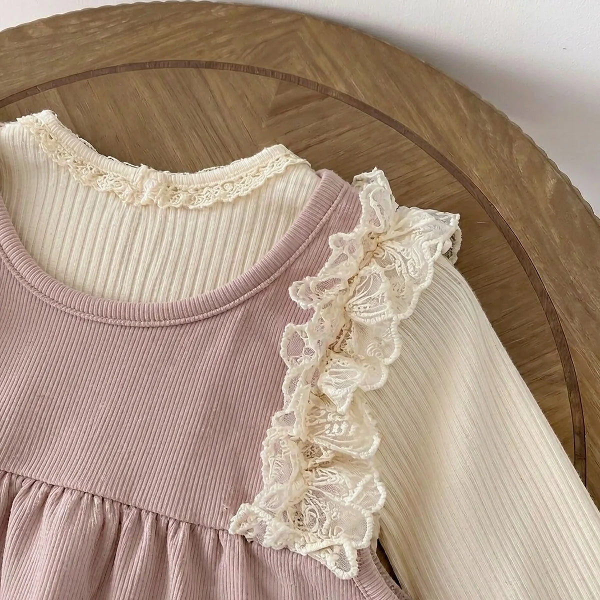 Close-up of white lace ruffle shoulder strap detail on the dusty pink ribbed baby romper