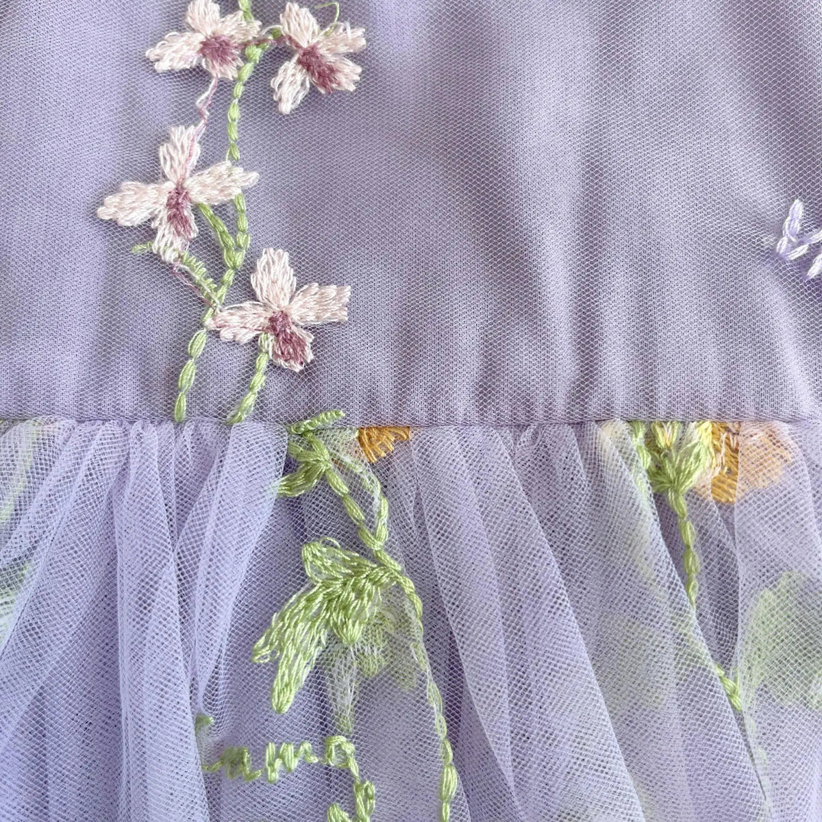 Close up of delicate floral embroidery on lavender tulle baby dress.