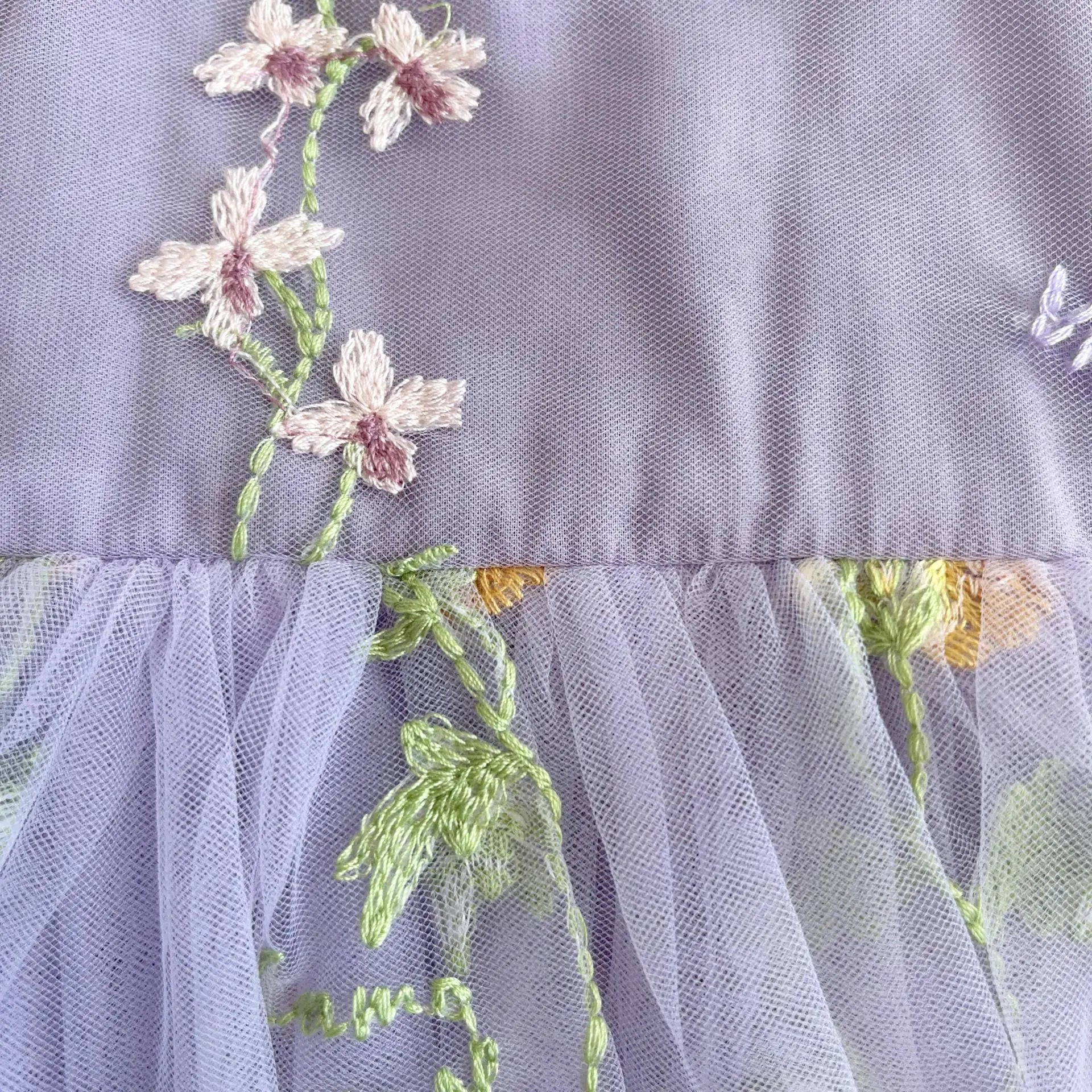 Close up of delicate floral embroidery on lavender tulle baby dress.