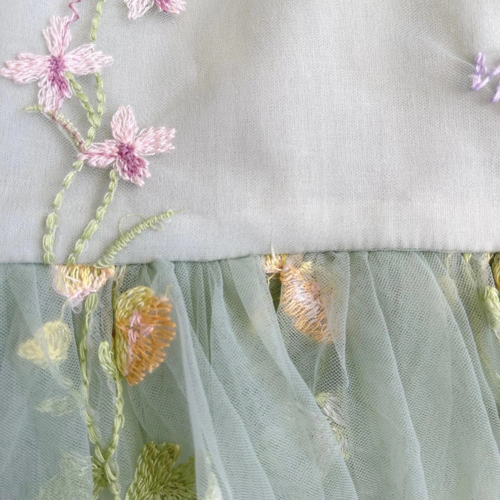 Close up of floral embroidery and tulle fabric on sage green baby romper.