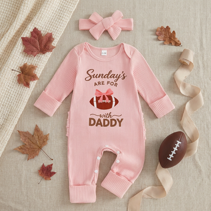 Flat lay of pink baby girl football romper and headband styled with autumn leaves and a miniature football.