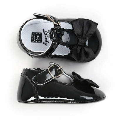Top-down and profile view of black patent baby dress shoes highlighting the cushioned white inner lining and anti-slip rubber walking sole.