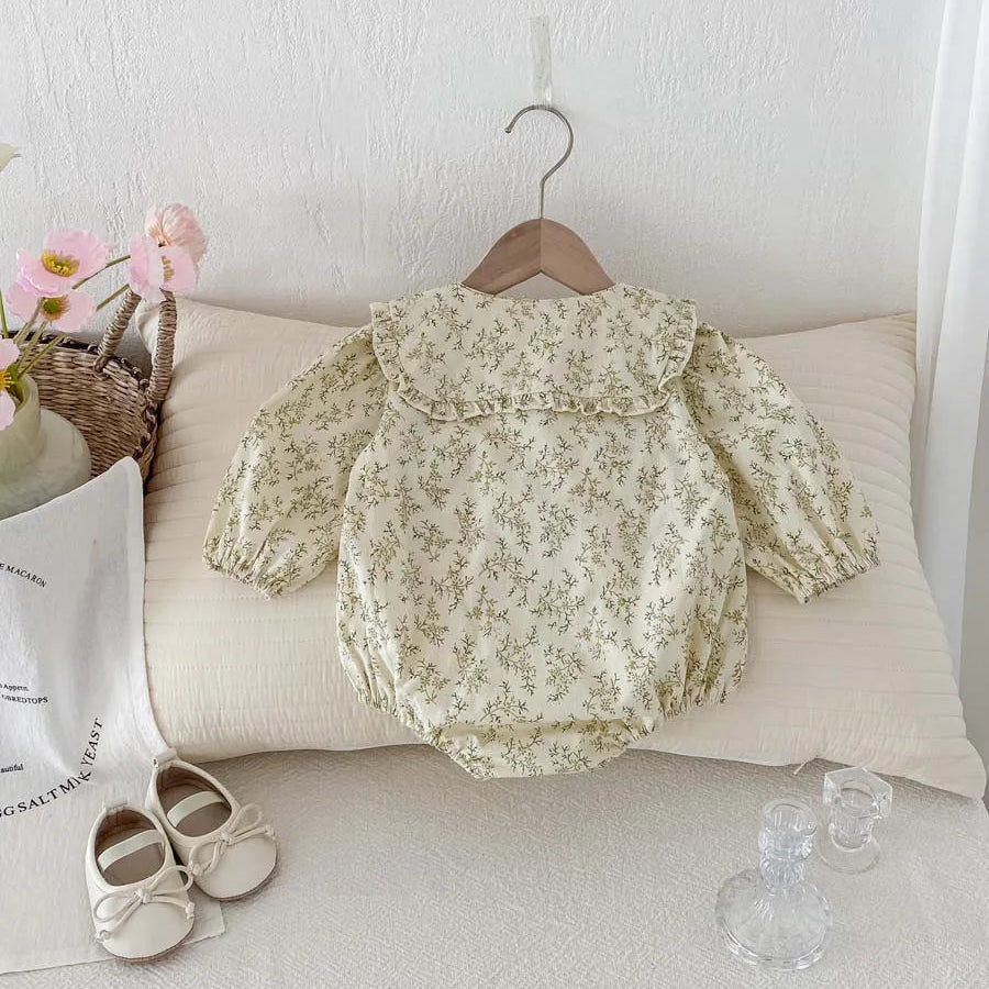 Kidsely vintage-inspired sage floral baby girl bubble romper displayed on a wooden hanger with decorative accessories.