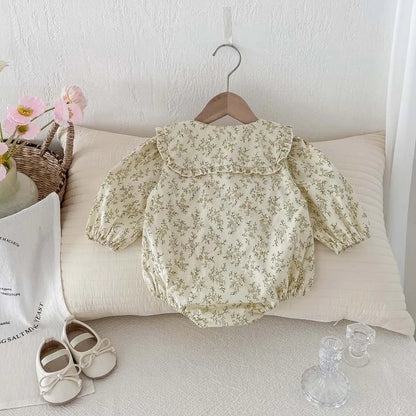 Kidsely vintage-inspired sage floral baby girl bubble romper displayed on a wooden hanger with decorative accessories.