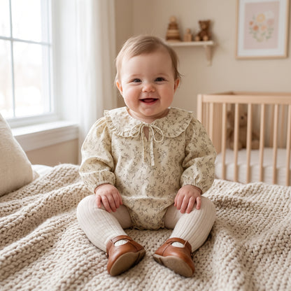 Baby girl sitting in a nursery wearing the Kidsely sage green cottagecore floral bubble romper paired with white tights.