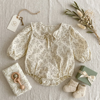 Styled flat lay featuring the Kidsely vintage-inspired floral baby girl romper alongside baby shoes, a rattle, and dried botanicals.