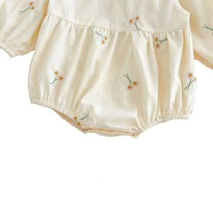 Close-up of bottom gathered leg openings and closed snap closure on cream baby girl romper