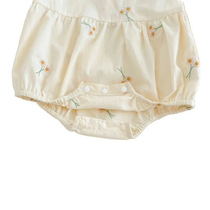 Close-up view of open bottom snap closures on cream baby girl embroidered bubble romper