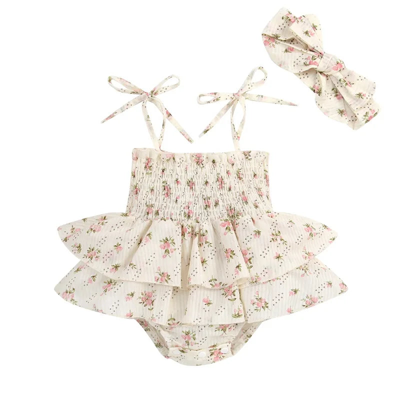 Flat lay of a baby girl's beige floral sleeveless romper with ruffled layers and a matching bow headband on a clean white background.