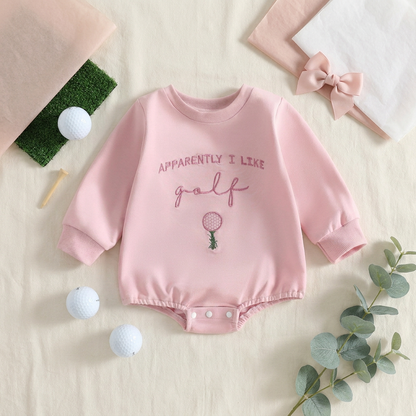 Flat lay style photo of the baby girl pink golf bubble romper styled with golf balls, tees, and a matching hair bow.