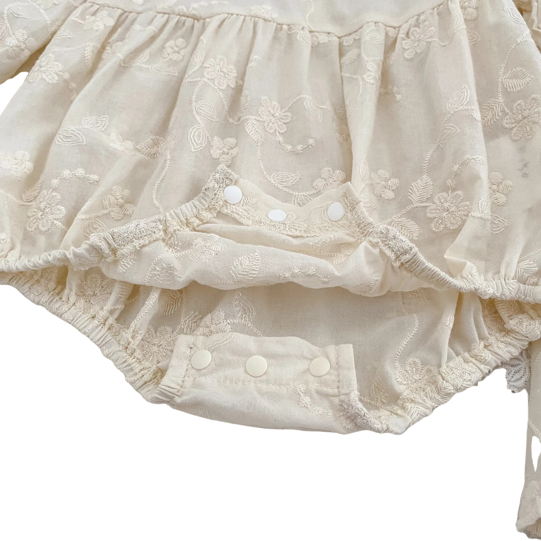 Detailed close-up of bottom snap button closures on baby girl ivory floral embroidered bubble romper.