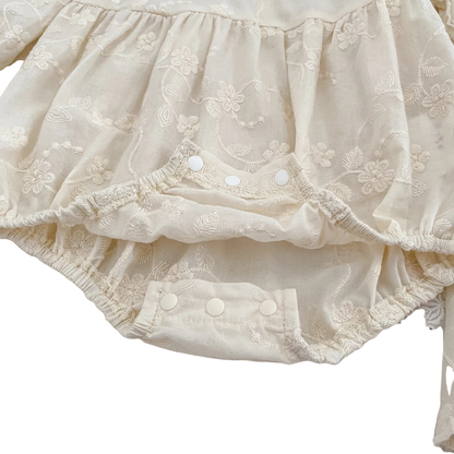 Detailed close-up of bottom snap button closures on baby girl ivory floral embroidered bubble romper.
