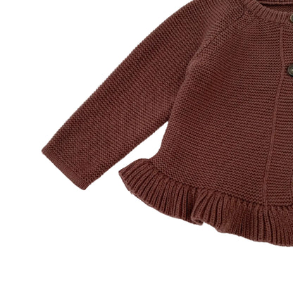 Close-up showing the long sleeve cuff and the textured ruffled hem detail on the bottom edge of the baby girl's brown knit sweater.
