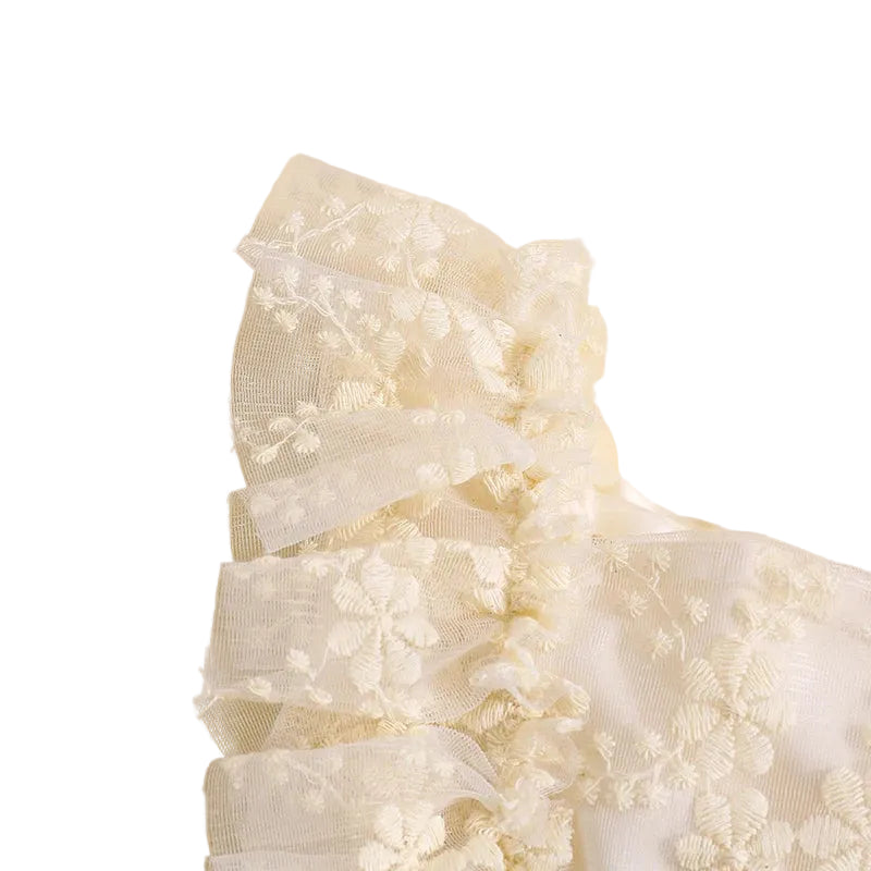 Close-up detail of delicate ruffle sleeve and layered floral lace fabric on cream romper
