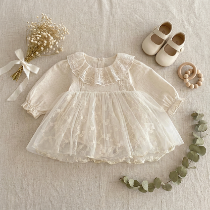 Flat lay of the baby girl lace romper dress styled beautifully with small white baby shoes, a pacifier clip, and dried floral accents.