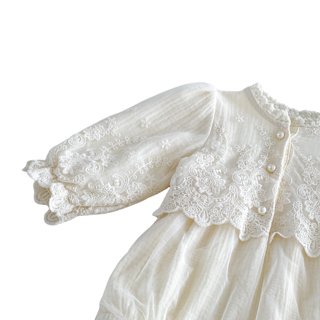Detailed view of long sleeves with ruffled lace cuffs and tulle overlay on an ivory baby girl bubble romper.