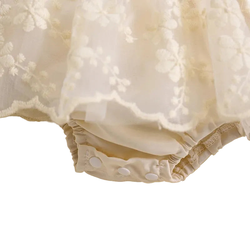 Close-up showing bottom snap closures on cream baby floral lace romper dress for easy diaper changes