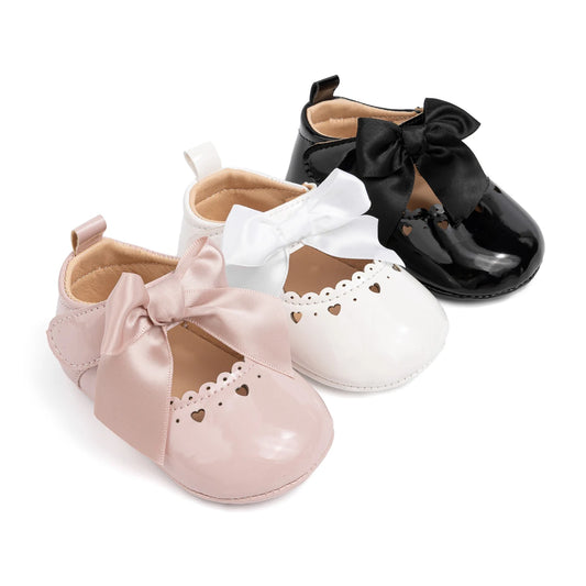 Three pairs of infant PU leather Mary Jane dress shoes shown side-by-side in soft pink, classic white, and glossy black colors.