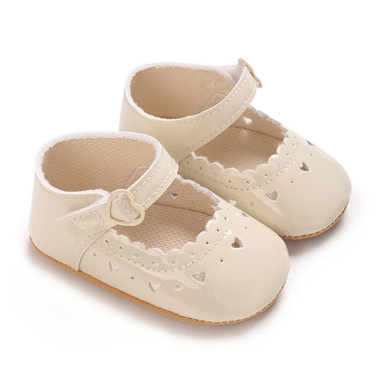 Pair of beige vegan leather baby girl Mary Jane shoes with heart cutouts and scalloped trim.