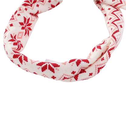 A knit headband with a red and pink Nordic snowflake pattern on a white background, shown against a plain white studio backdrop.