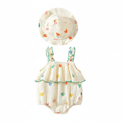 Flat lay of a white muslin cotton baby girl romper with colorful heart prints, ruffle straps, and a matching wide-brim sun hat on a clean white background.