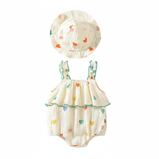 Flat lay of a white muslin cotton baby girl romper with colorful heart prints, ruffle straps, and a matching wide-brim sun hat on a clean white background.