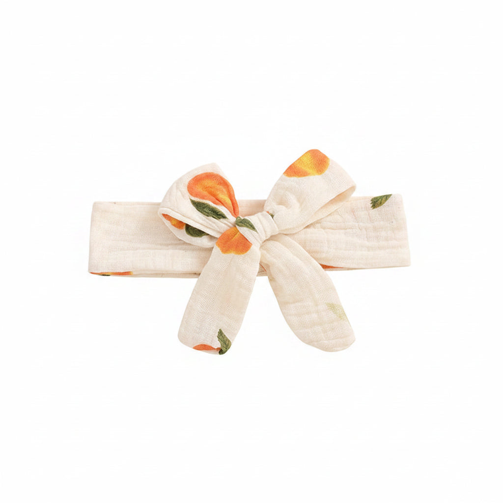 Matching baby girl bow headband in white with orange peach print and soft elastic band.