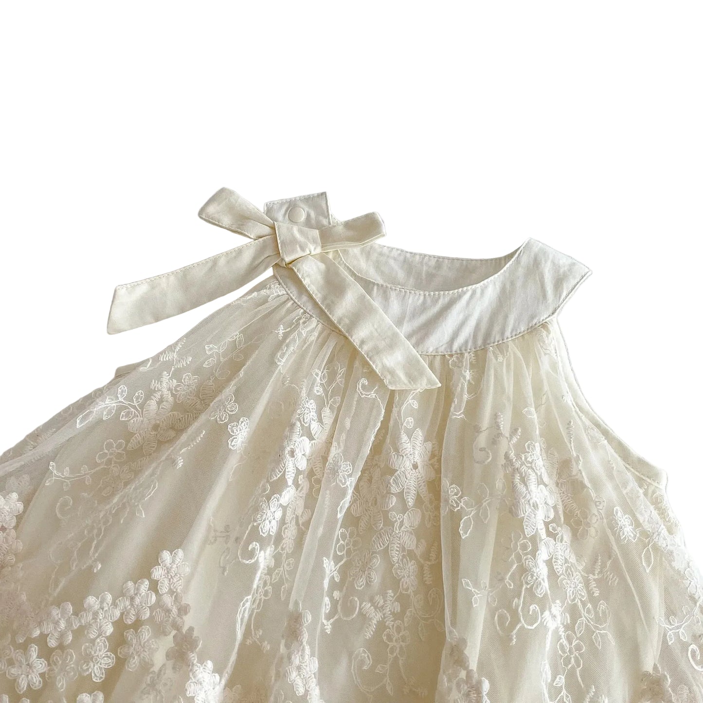 Top-down angled shot focusing on the neckline, collar stitch detail, and shoulder bow tie of the Pearl Ivory infant romper dress.