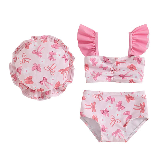 Three-piece baby girl swimsuit set featuring a soft pink bow print ruffle tankini, swim shorts, and matching sun hat.