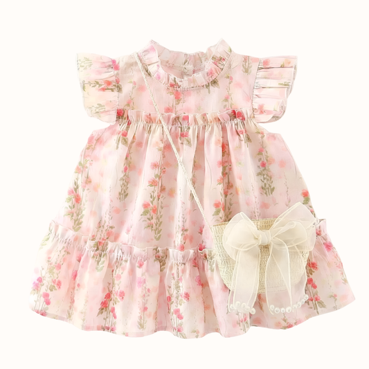 Flat lay of a baby girl's pink floral cotton princess dress with ruffle fly sleeves and a matching straw-weave crossbody bag with a large organza bow on a white background.