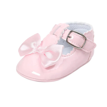 Side angle view of a single baby girl pastel pink patent leather T-strap Mary Jane dress shoe featuring a matching pink satin bow.