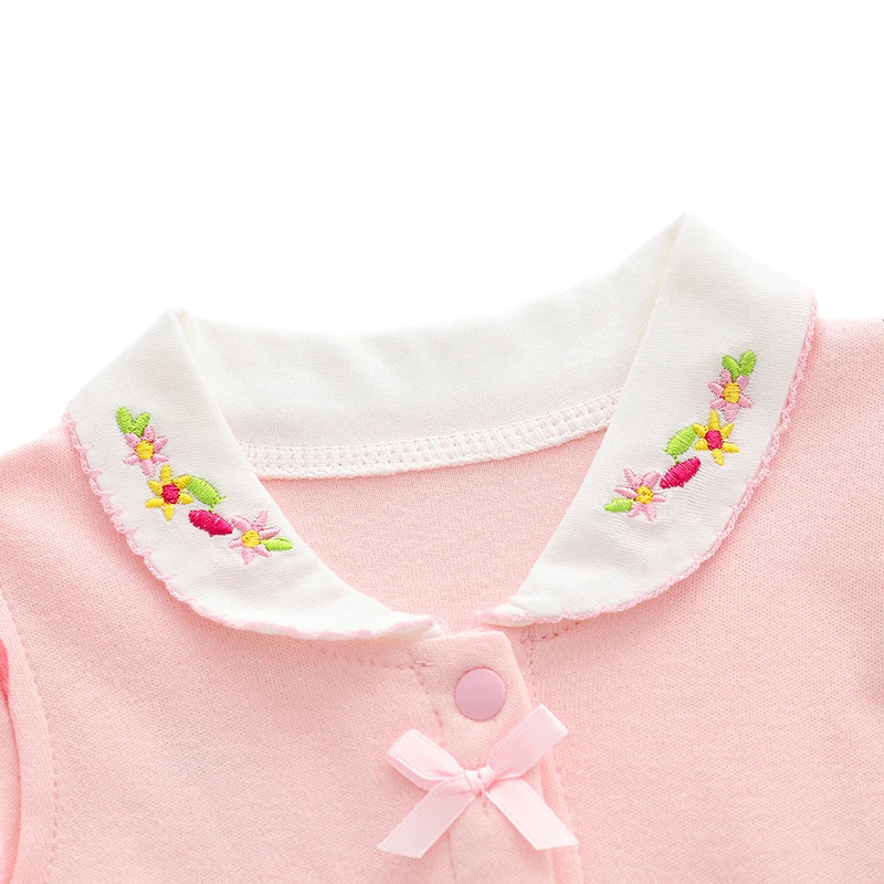 Detailed close-up of the white Peter Pan collar featuring colorful floral embroidery and a small pink decorative fabric bow on the top snap button.