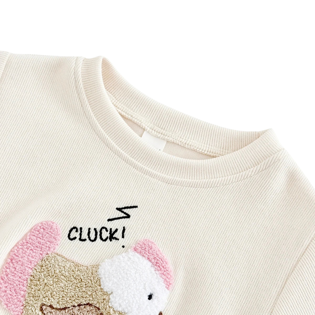 Close-up view of the soft off-white knit sweatshirt collar and embroidered chicken applique with "CLUCK!" detail.