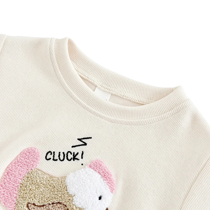 Close-up view of the soft off-white knit sweatshirt collar and embroidered chicken applique with "CLUCK!" detail.