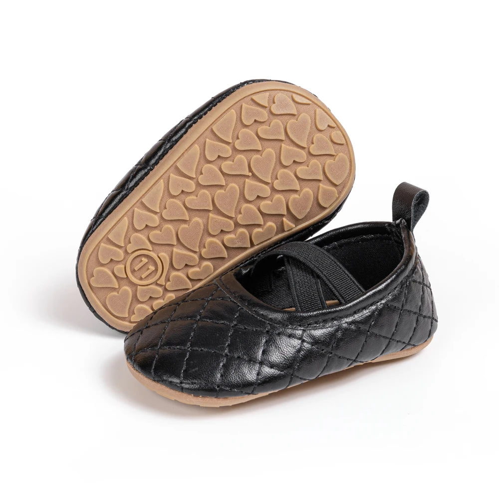 Angle view of a pair of Kidsely black quilted baby girl Mary Janes, showcasing the heart-patterned non-slip sole.
