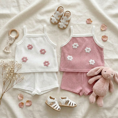 Beautiful aesthetic boutique display featuring both petal white and dusty rose pink ribbed sets styled on a textured background with baby shoes, sunglasses, and a plush bunny toy.