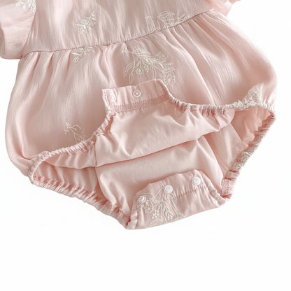 Detail view of the three reinforced snap buttons at the bottom of a pink cotton romper for easy diaper changes.