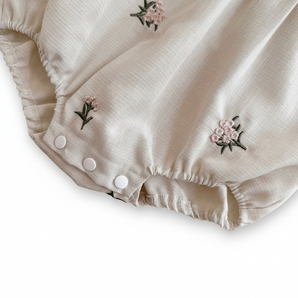 Close-up view of the white bottom snap closures and gathered elastic leg openings on the baby girl romper.